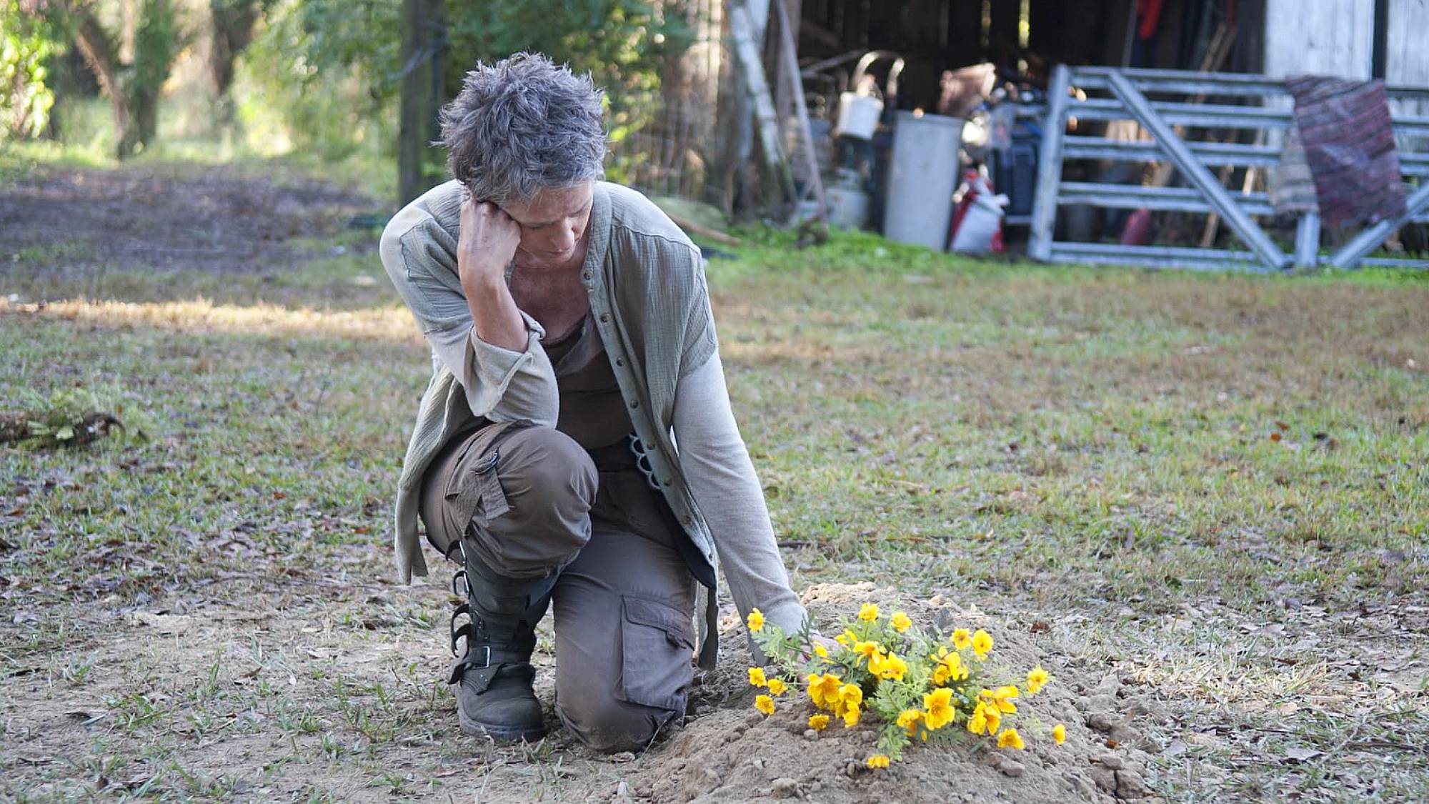 Melissa McBride as Carol, kneeling beside some yellow flowers in "The Walking Dead" season 4 episode 14, titled "The Grove"