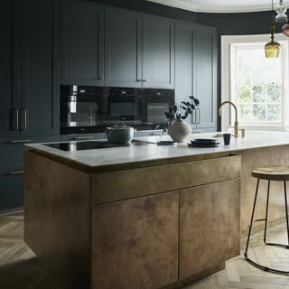 kitchen with island in aged brass and black-green cabinets behind
