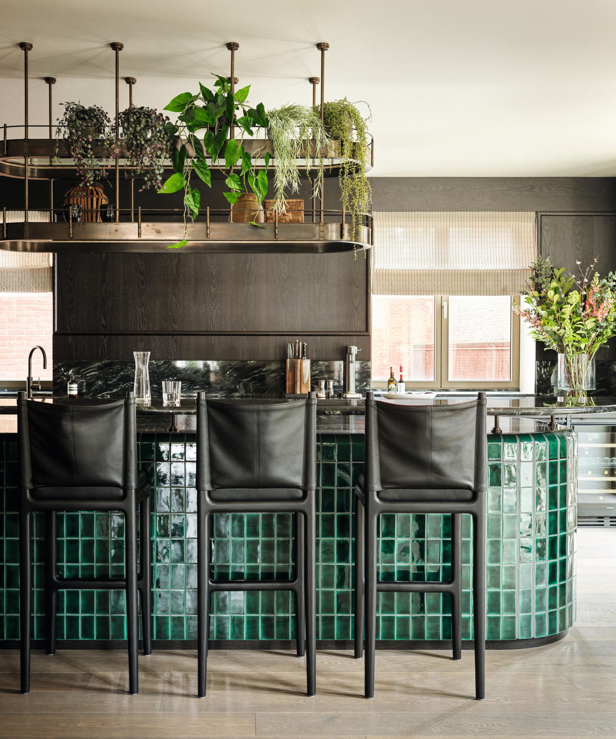 a modern kitchen with a large green tiled kitchen island with a hanging shelf display styled with plants