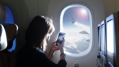Woman taking a photo of sky from airplane seat