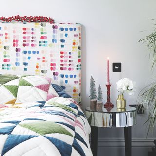 White painted bedroom with a colourful headboard and a colourful duvet set, with Christmas decorations on the bedside table