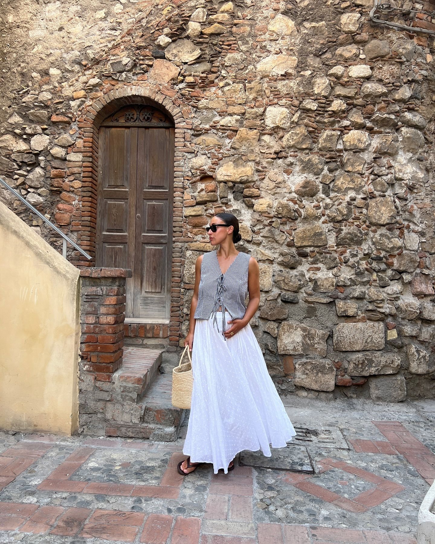 Woman wears gingham top and white skirt and black sandals