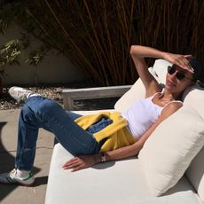 @tylynnngyuen sitting on white couch outside wearing white tank top, jeans, and yellow sweater tied around waist