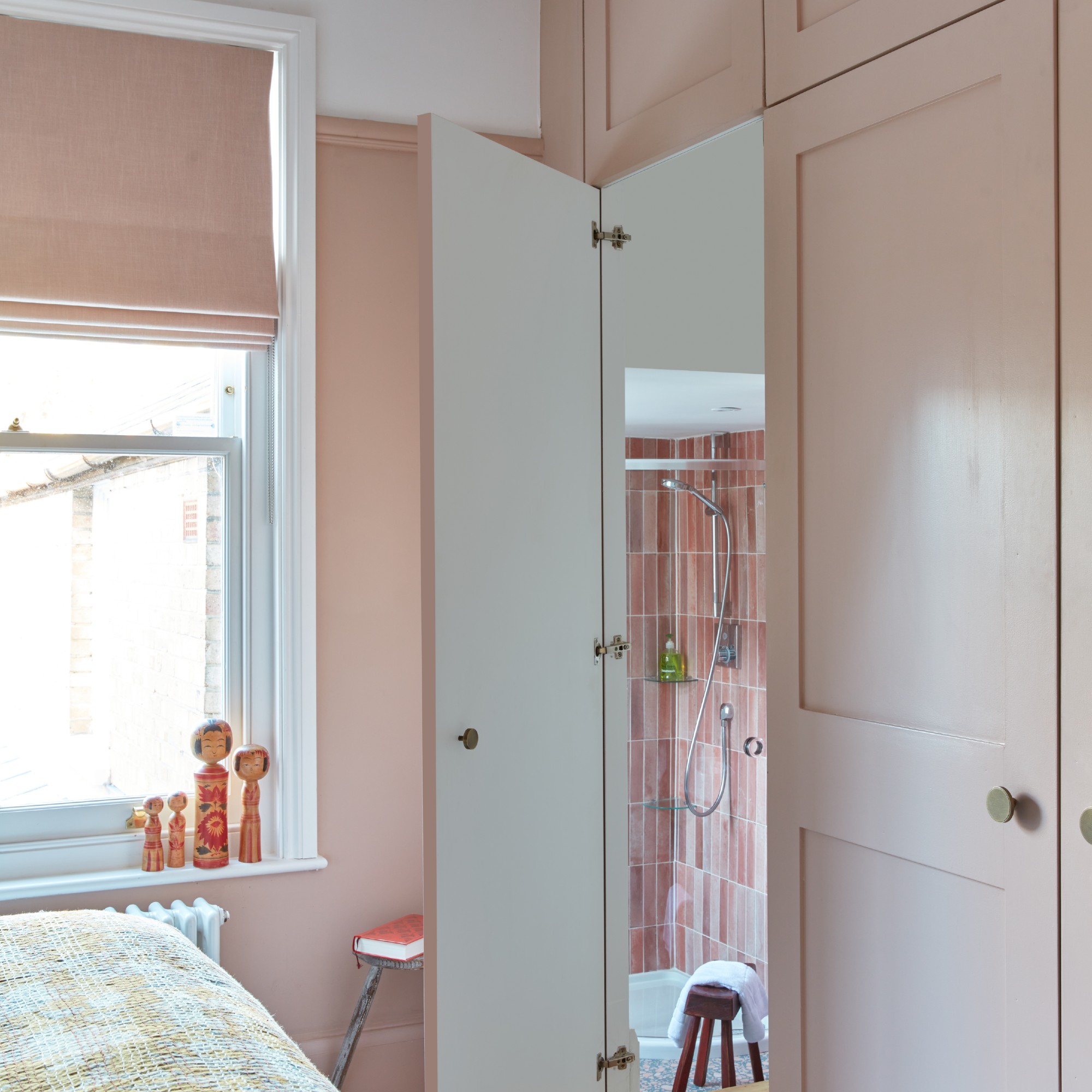 A small light pink bedroom with built-in wardrobes and an ensuite pink bathroom
