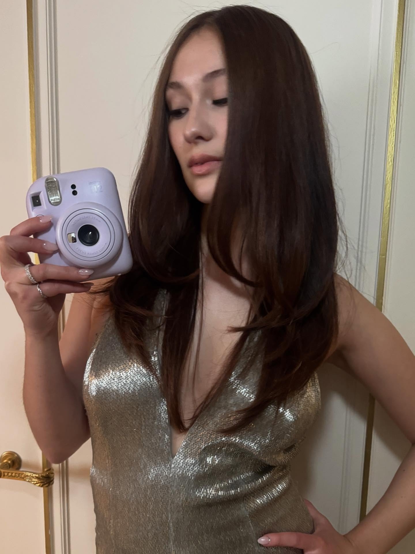 Lola Tung with sleek medium brown hair, taking selfie with a Polaroid camera