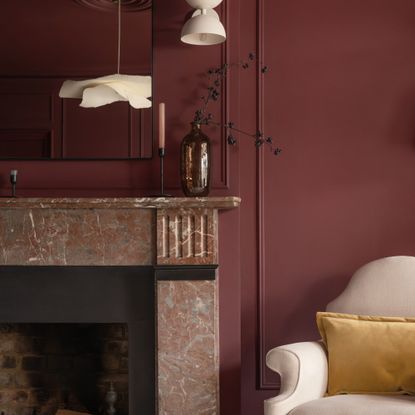 A living room colour drenched in Lick's Red 06 shade with a tonal marble fireplace and a cream chair