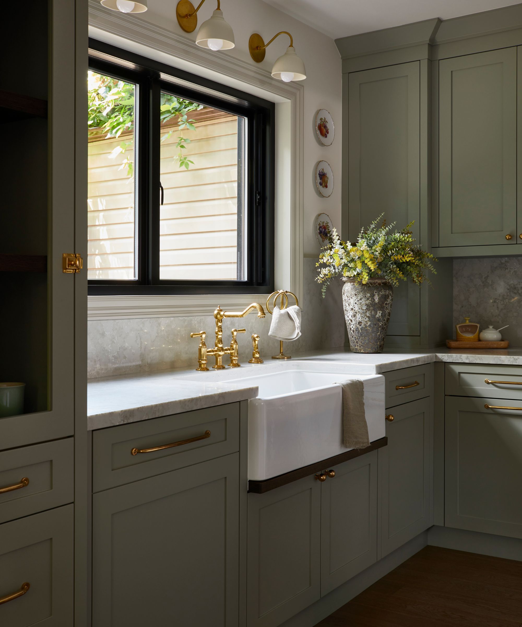 a sage green shaker kitchen sink area with a farmhouse sink and a large window dressed with sconces and wall plates