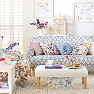 White living room with blue patterned sofa and floral print sofa and white window shutters