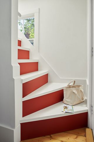 A staircase painted in a red and white shades with a canvas bag and an open magazine placed on the bottom step