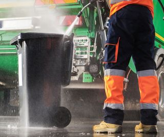 A man pressure washing a garbage can