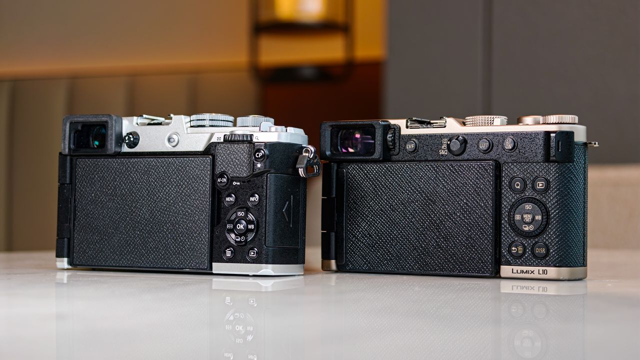 OM System PEN vs Panasonic Lumix L10: two micro four thirds cameras side by side on a white marble surface with lamp light in the background