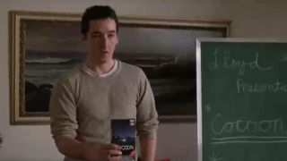 John Cusack standing in front of a chalkboard, holding a VHS tape of Cocoon in Say Anything.