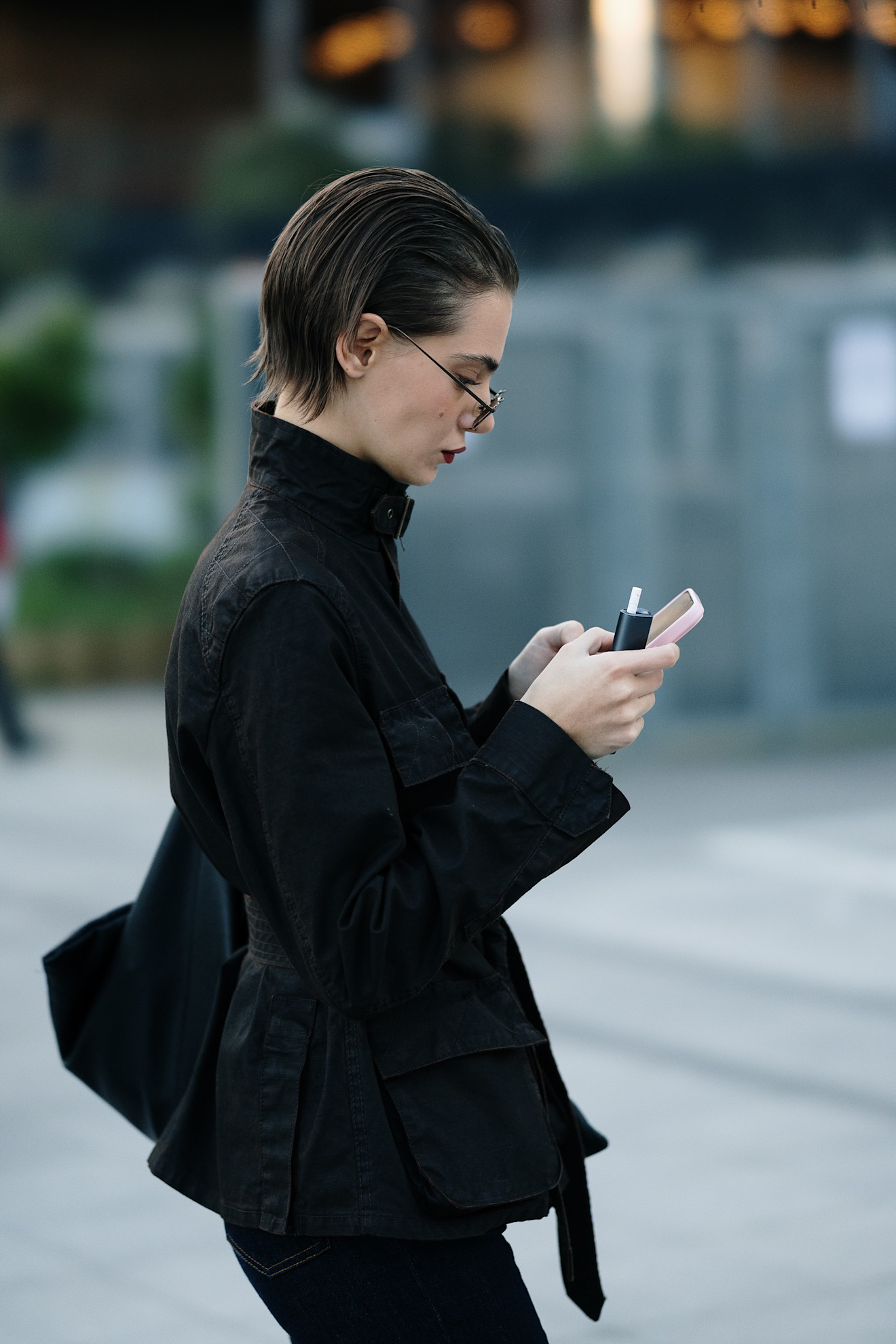 A woman with a short brown bob in profile with a black jacket texting