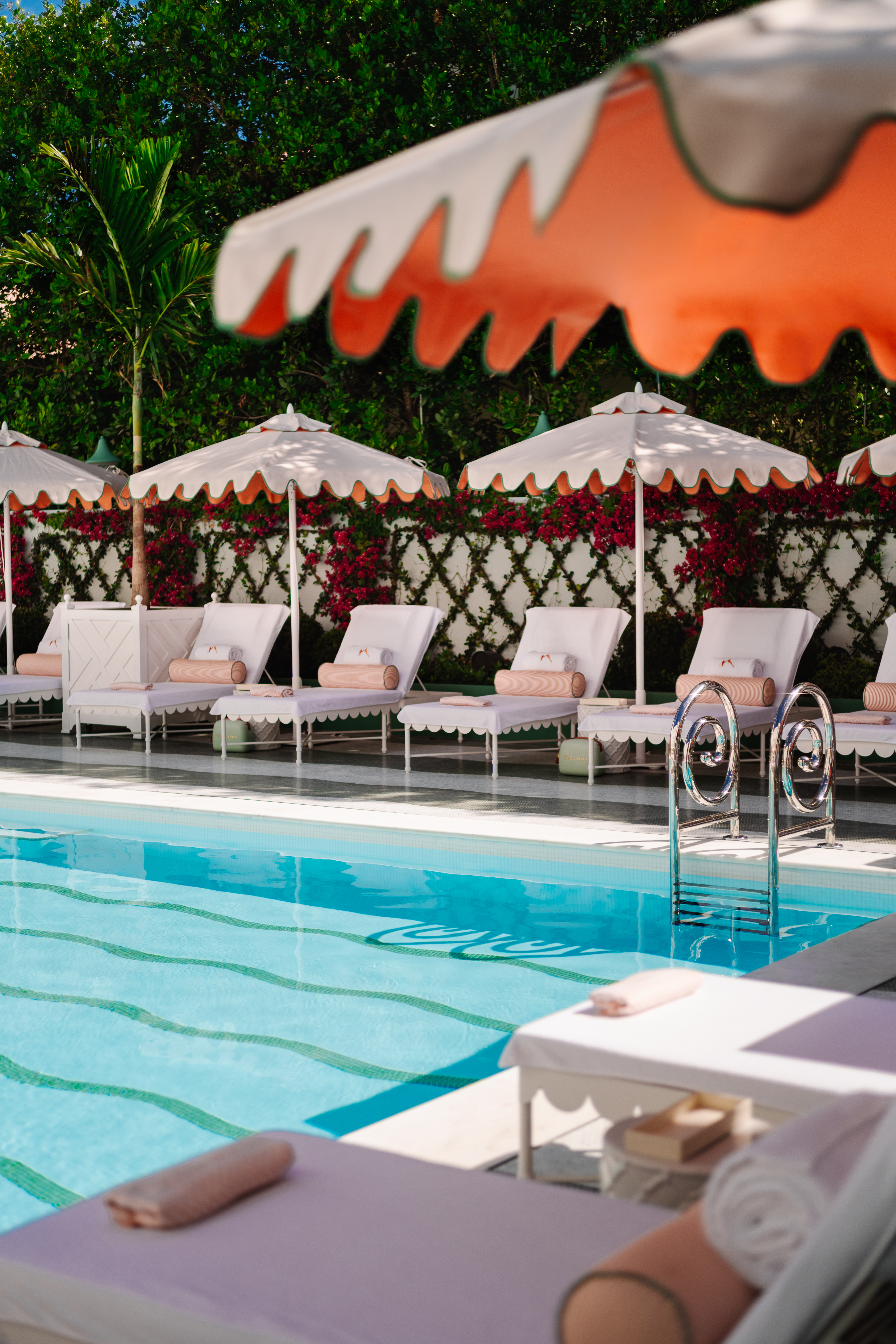Swimming pool with turquoise tiles and green squiggle line detail surrounded by white, scalloped sun beds