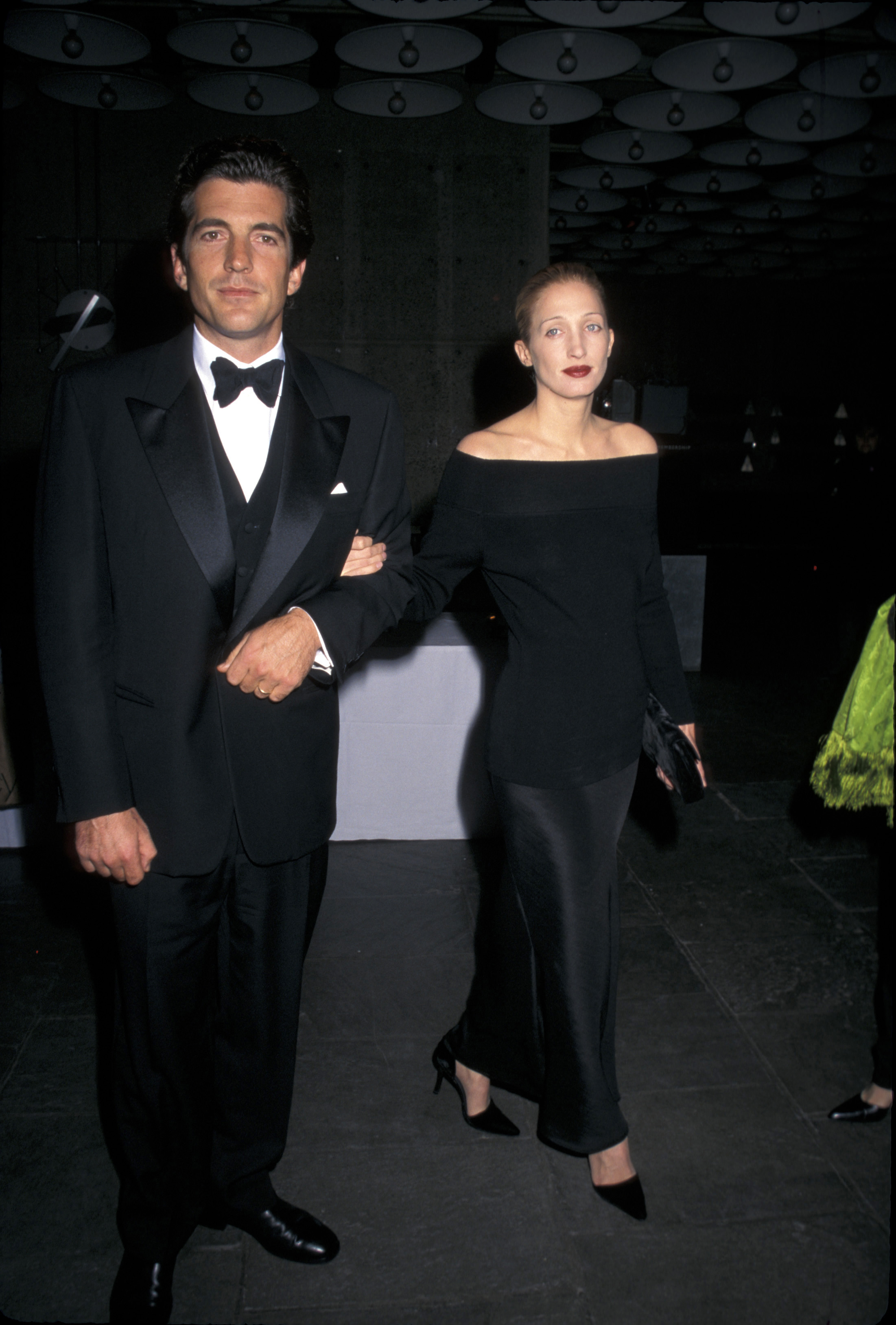 Carolyn Bessette-Kennedy wearing an off-the-shoulder top, a black slip skirt, and black heels