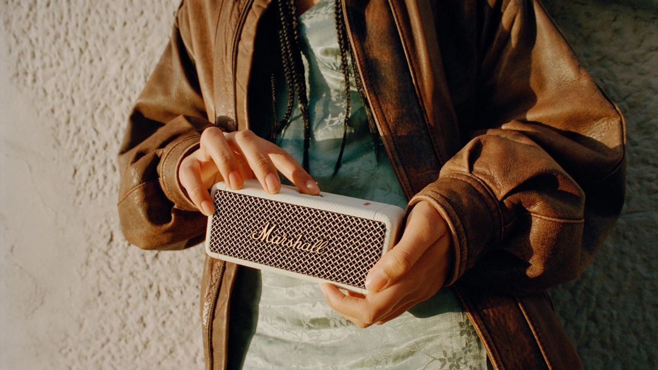 Girl with tan leather jacket holding Marshall emberton ii speaker