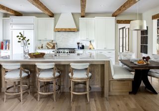 farmhouse style kitchen with beams, white cabinets, wood island with table on one end, bar stools, hardwood floor, sink in island