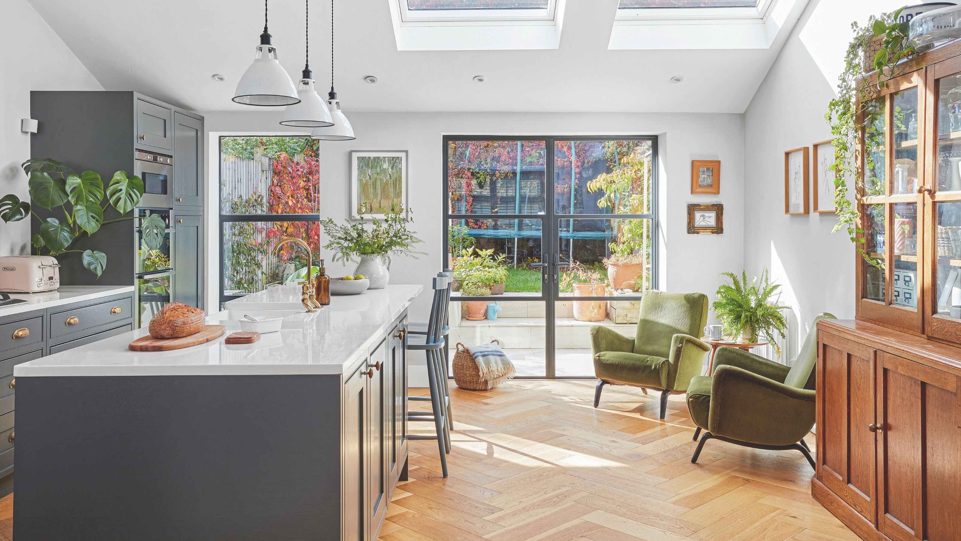 Open plan kitchen and living space with dark grey cabinets and a kitchen island, with accent chairs in the space beside it