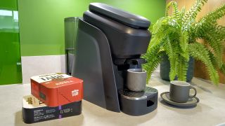 Lavazza Tabli coffee maker on kitchen counter with coffee tabs and espresso cups, and a boston fern plant