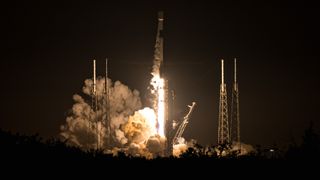 a black-and-white spacex falcon 9 rocket launches into a night sky.