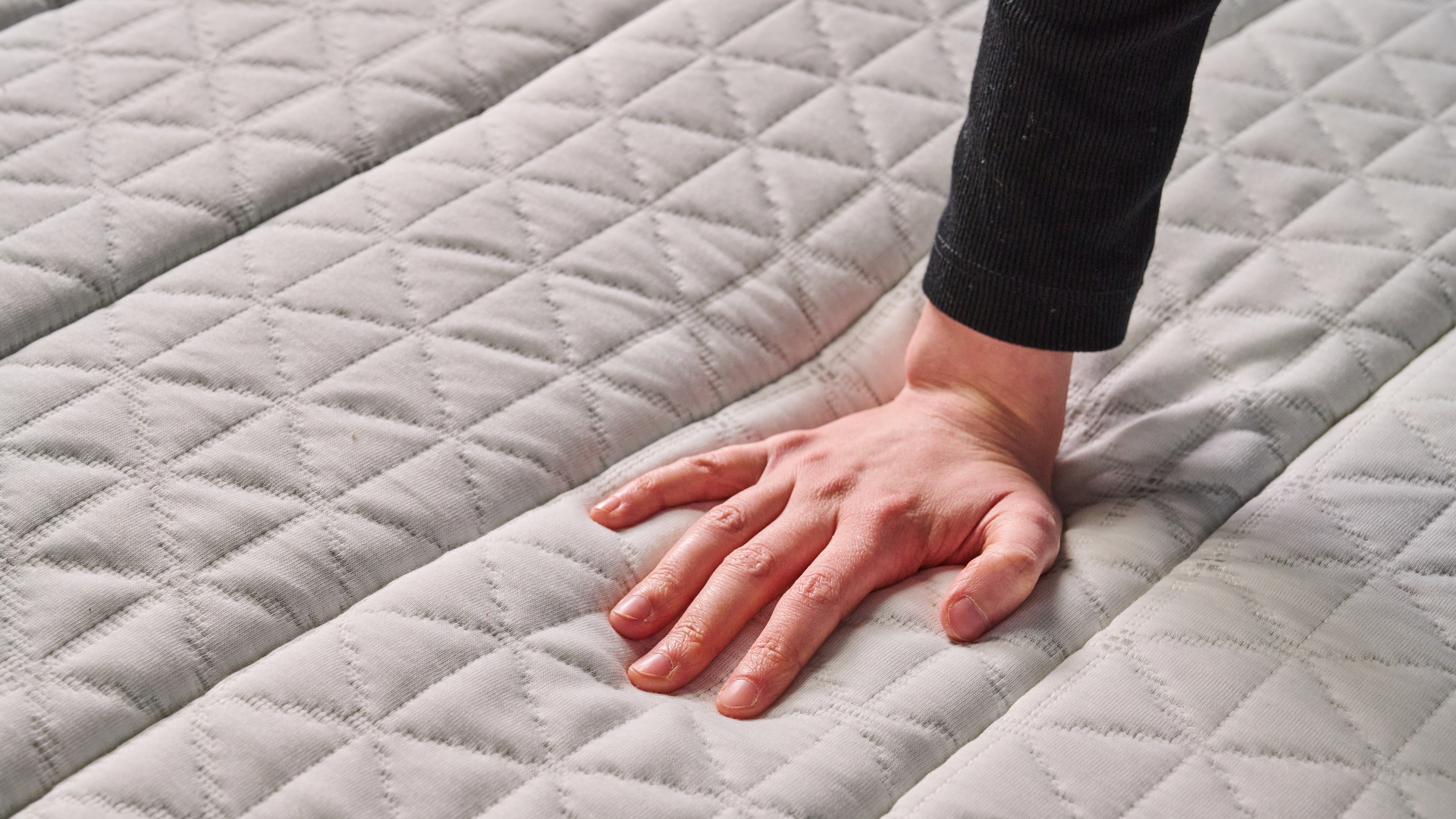 A hand feels the firmness of the Helix Midnight Mattress, a bed designed for side sleepers.