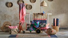Image of a concrete room with a lot of different colorful, woven homeware items arranged in a product display way. There are rugs, baskets, wall hangings, pillows, and blankets.