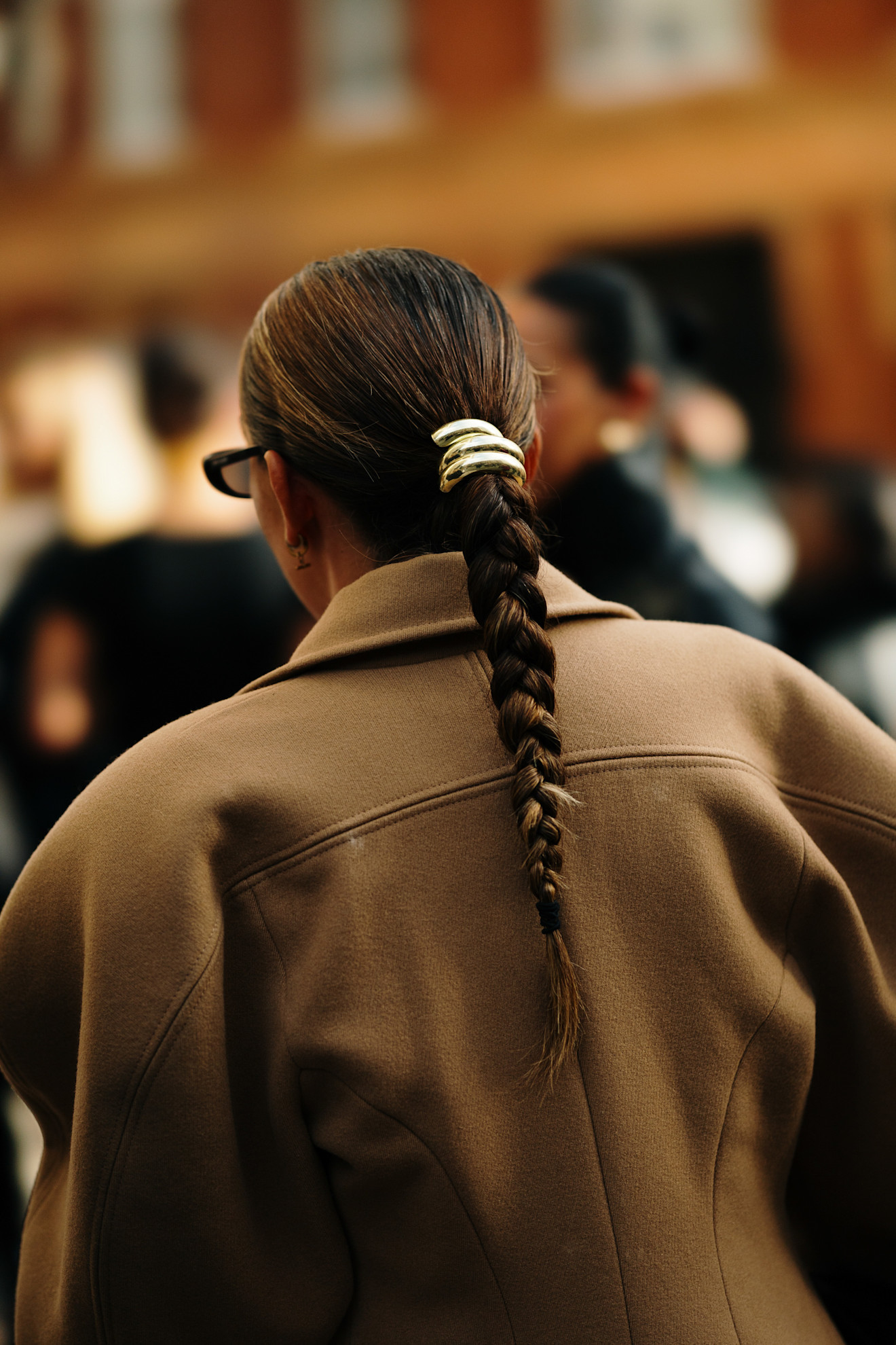 a close up of a woman with a brown braided ponytail from the back with a silver cuff, olive green jacket