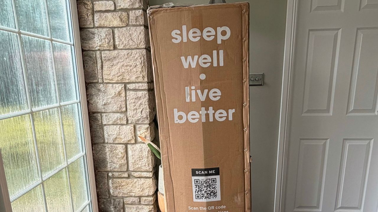 A tall and slightly battered brown box with the words 'Sleep well. Live better' printed in white on the side, placed inside an entrance hall