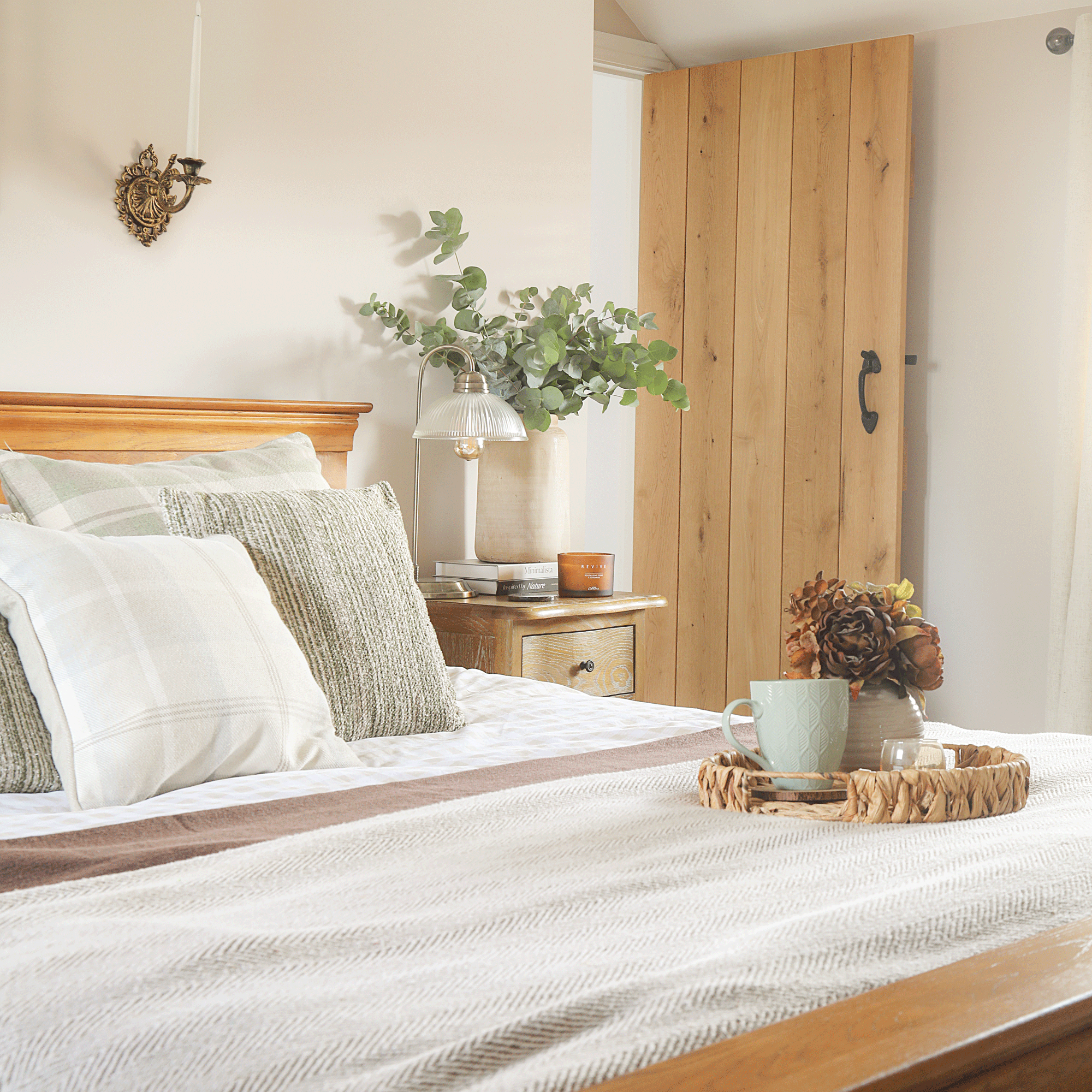 A neutral bedroom with textured white and cream bedlinen and a tray on the bed with a mug and vase