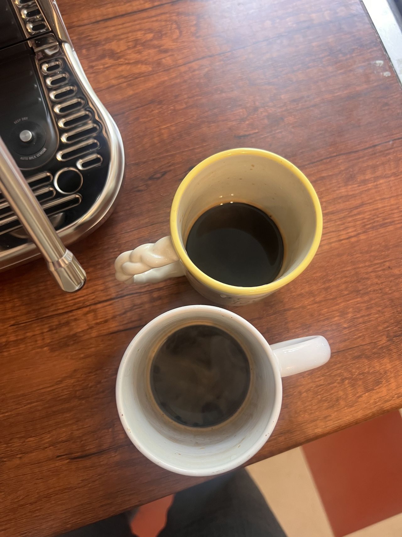 Image of two coffee mugs with a shot of espresso in them on a wooden countertop.