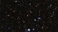  Hundreds of galaxies appear in this view, which is set against the black background of space. There are many overlapping objects at various distances. They include large, blue foreground stars, some with eight diffraction spikes, and white and pink spiral and elliptical galaxies. Numerous tiny orange dots appear throughout the scene