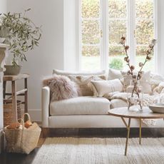 Autumnal, neutral living room with a cream sofa covered in cushions and a storage basket full of wood on the left