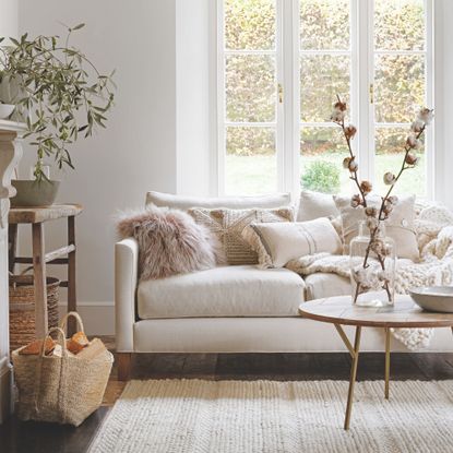 Autumnal, neutral living room with a cream sofa covered in cushions and a storage basket full of wood on the left
