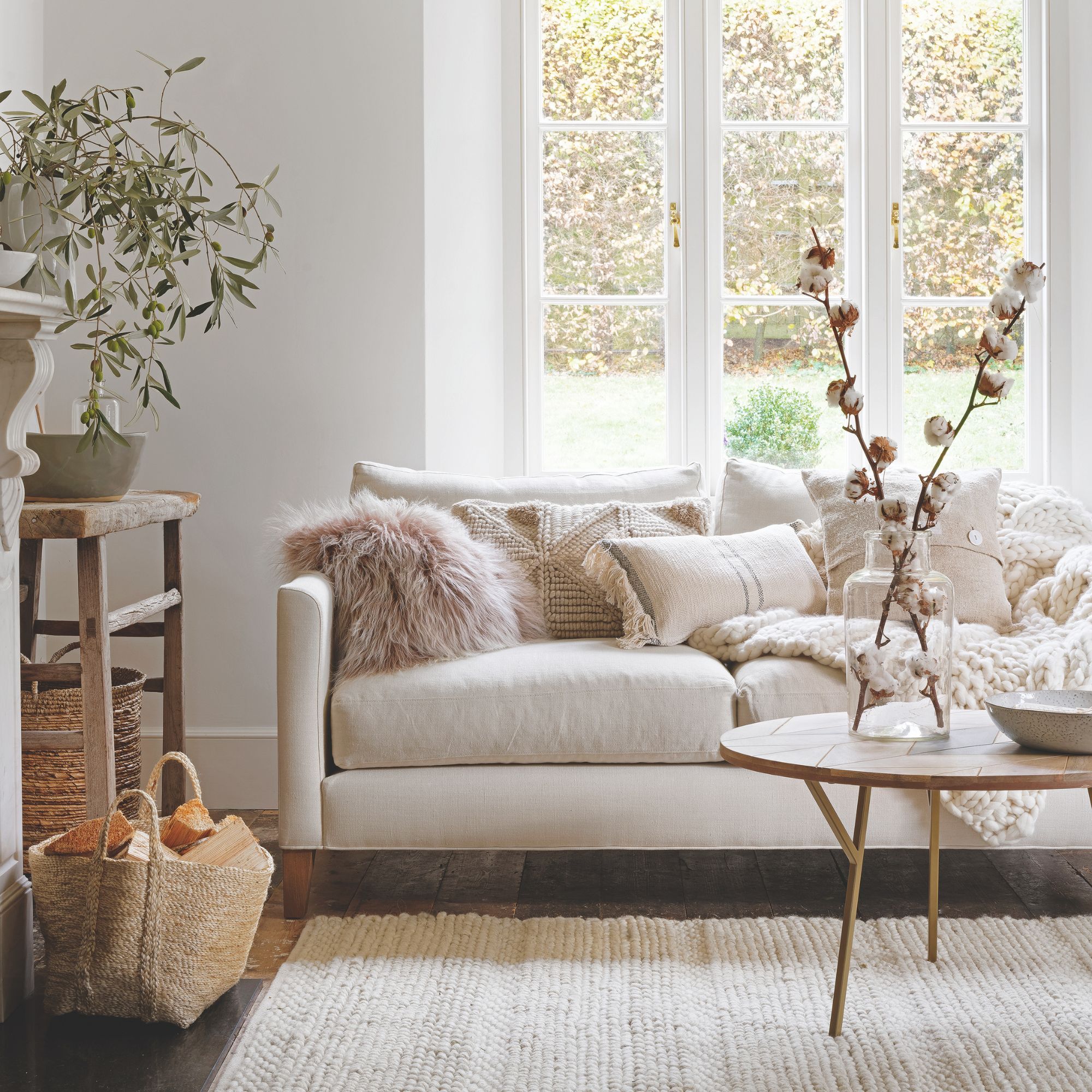 Autumnal, neutral living room with a cream sofa covered in cushions and a storage basket full of wood on the left