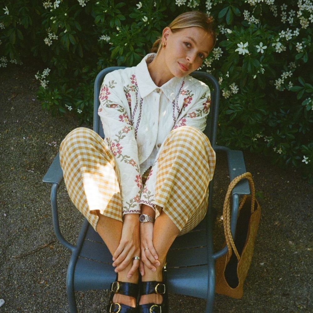 Influencer wears yellow gingham trousers with a white, floral embroidered shirt and gold-buckle sandals.