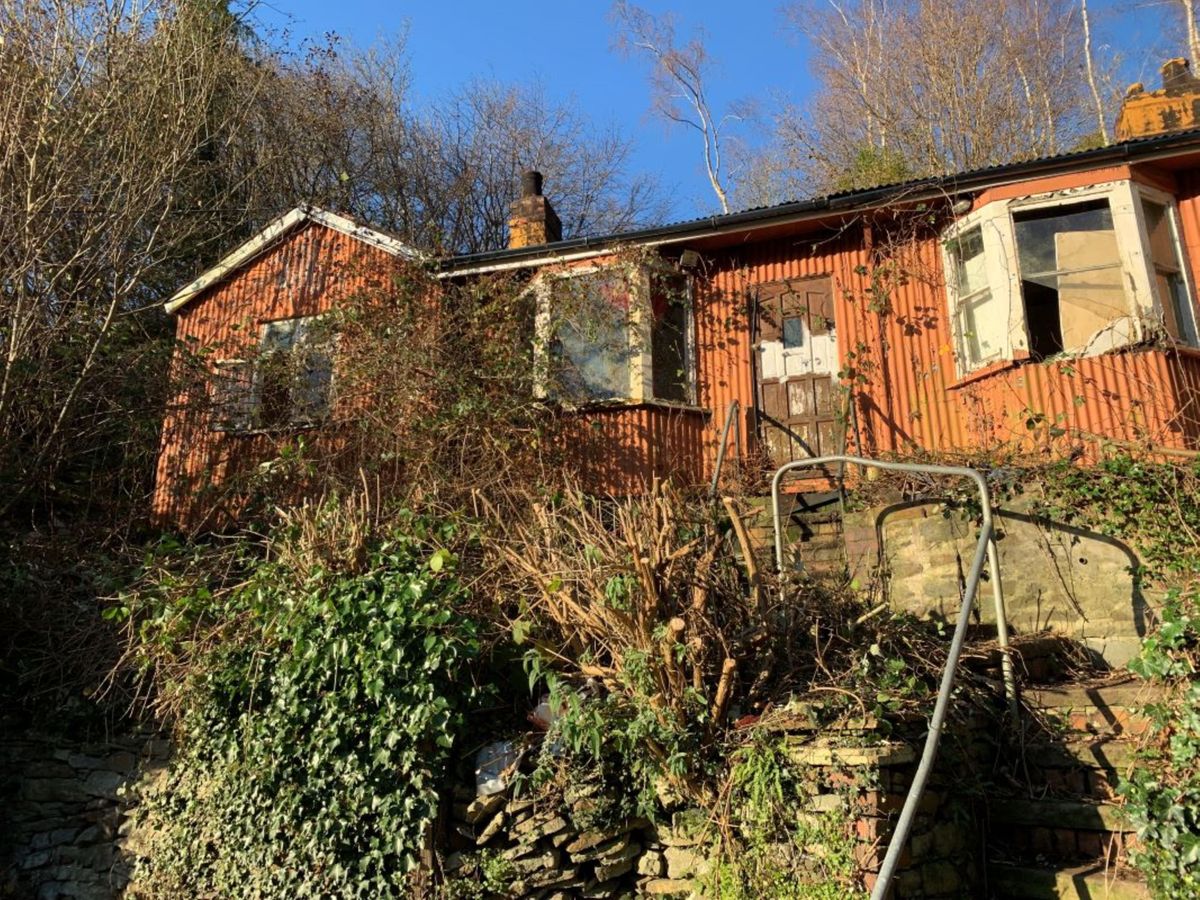 A dilapidated bungalow on a hill with bramble all around