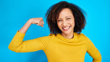 A woman flexes one arm and smiles.