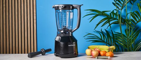 a black nutribullet with a big blending component is photographed in front of a blue backdrop, showing its plastic pitcher jug, silver blades, and tamper