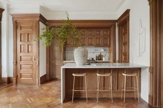 A wooden panelled kitchen with a marble top island in an otherwise whitye space