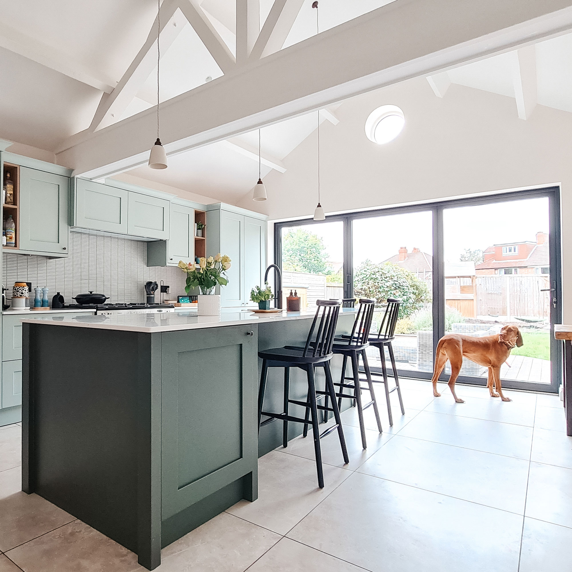 Green kitchen cabinets with black bar stools around kitchen island