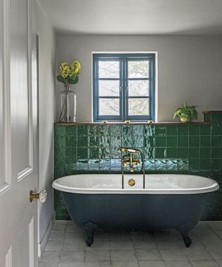 Bold green wall tiles behind a dark green free-standing bath