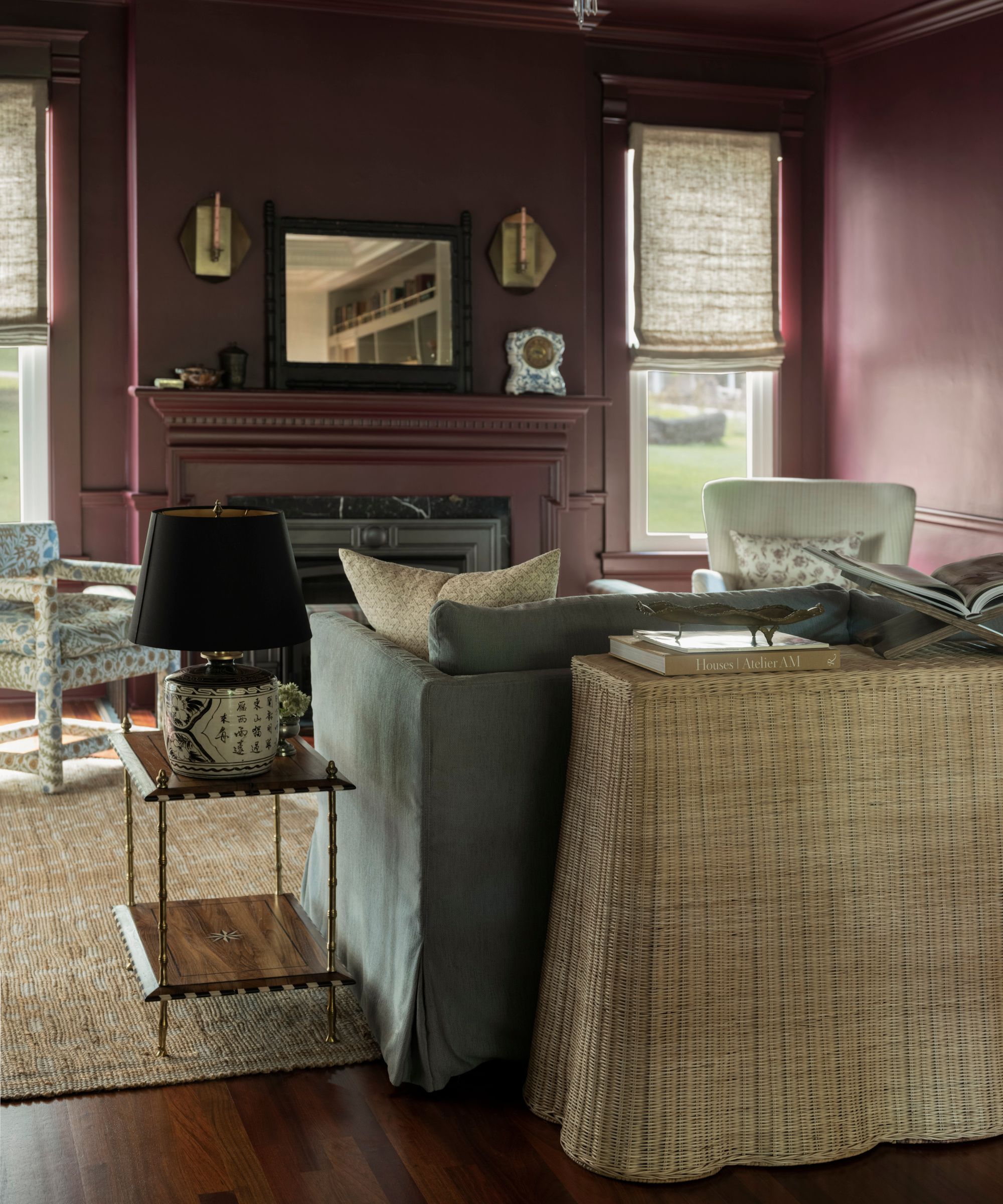 dark reddy purple color drenched living room dressed with a light blue couch, leather ottoman, floral armchairs and drapes and a large wicker console