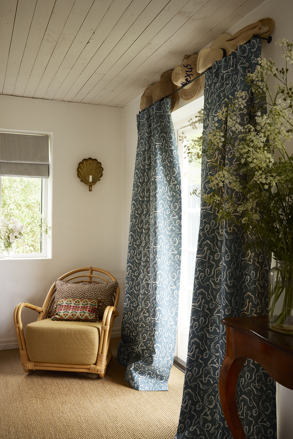 scandinavian coastal interior with white timber panel ceiling, sisal carpet, patterned curtains, rattan armchair in corner with patterned cushion