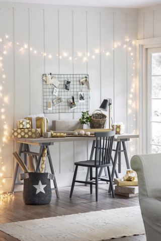 Christmas cards displayed on wire memo board with grey wooden desk, chair and fairy lights