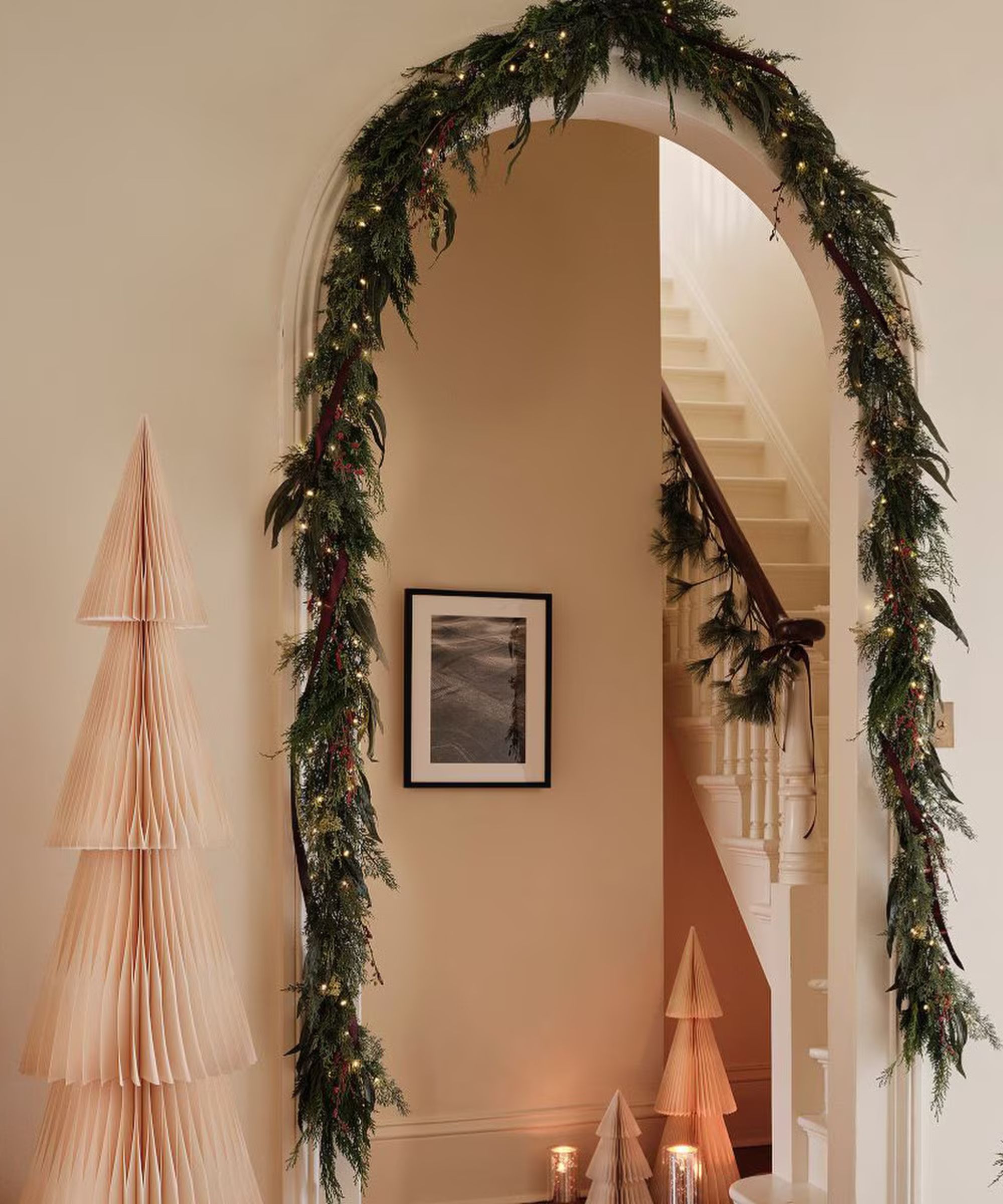 Entryway decorated for Christmas with a garland over an arched door and a paper Christmas tree