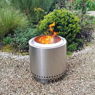 The stainless steel Solo Stove Ranger fire pit burning in a gravel garden
