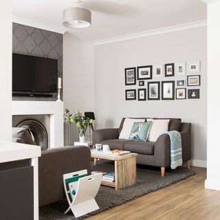 living room with white walls contains wallpaper with television and has grey sofa set