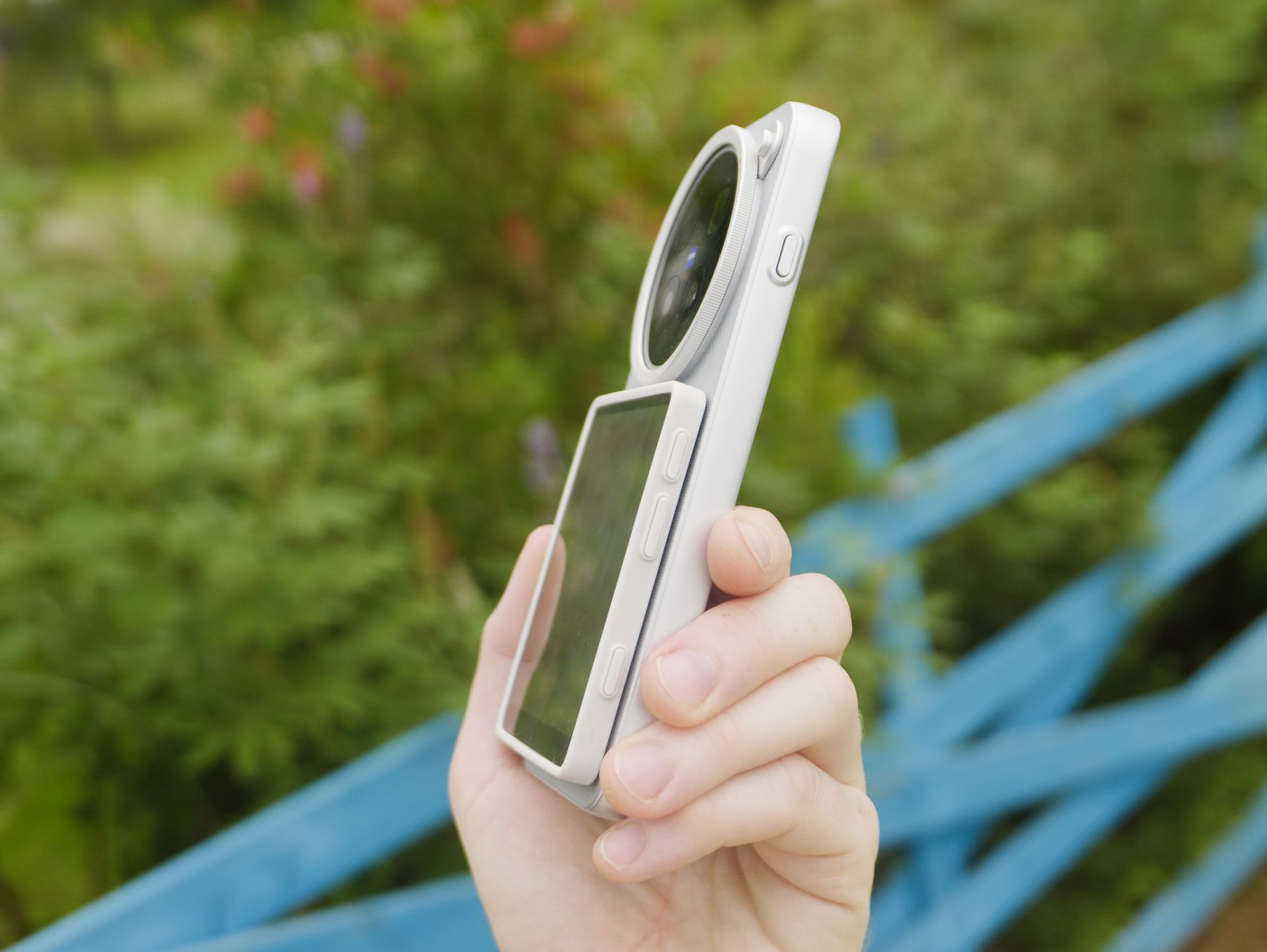 The Vivo X500 Pro Max phone in user's hand, in its dedicated case for magnetic accessories, with Vivo's selfie screen attached, side profile to show how thin the combo are