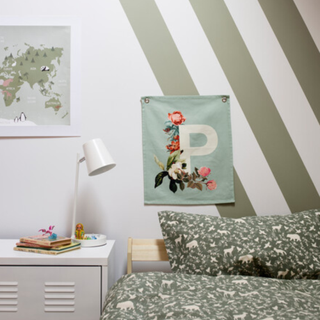 A bedroom painted with green and white diagonal stripes on the wall, with green floral bedding and a white bedside lamp