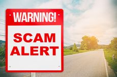 A warning sign warning about Scam in road ahead.